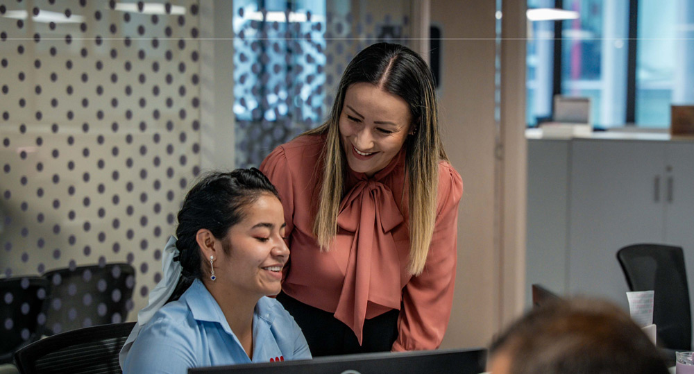 Mujeres sonriendo frente a una pantalla en la oficina