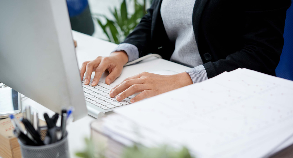 Manos escribiendo en teclado y revisando documentos